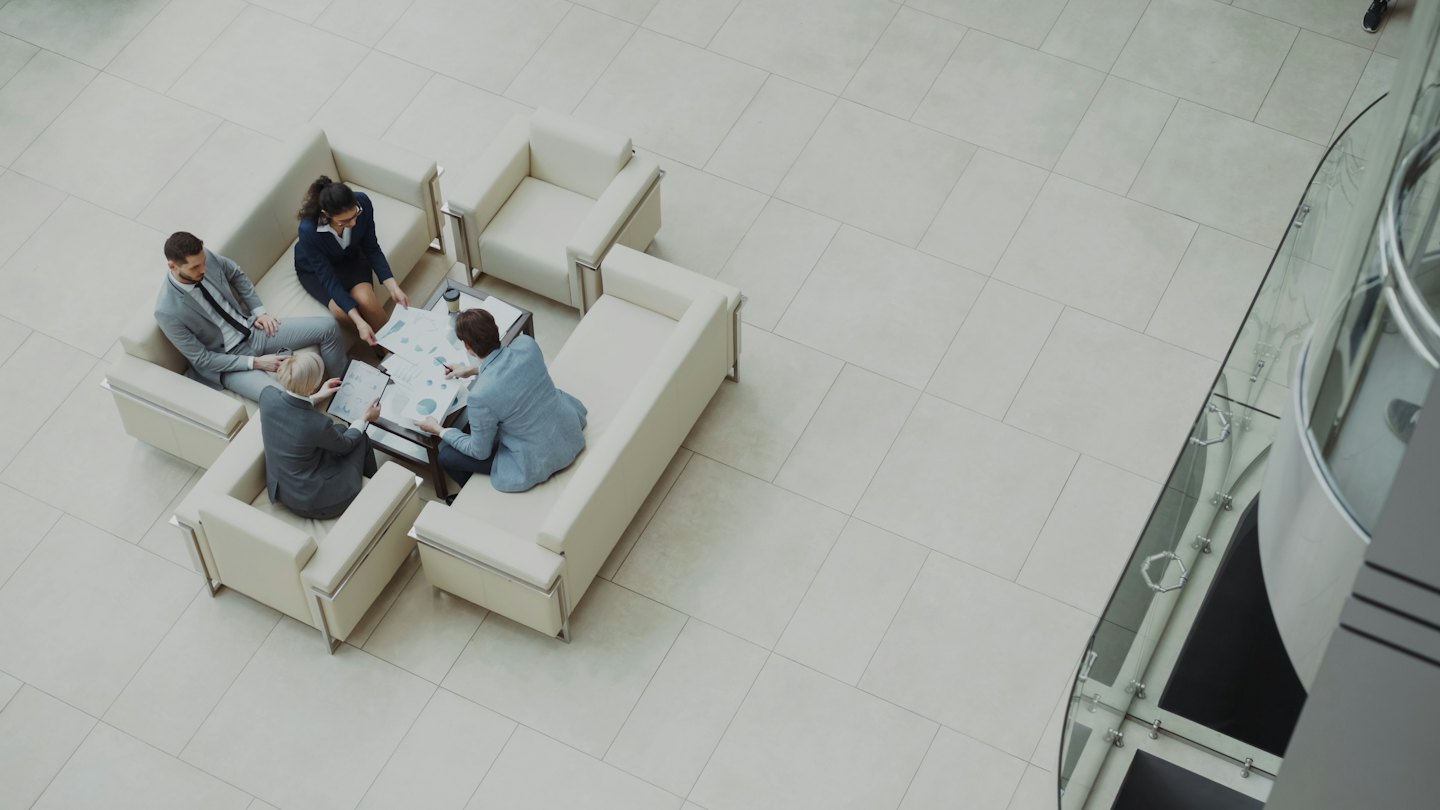 Cuatro profesionales en un vestíbulo de oficina revisando documentos alrededor de una mesa.